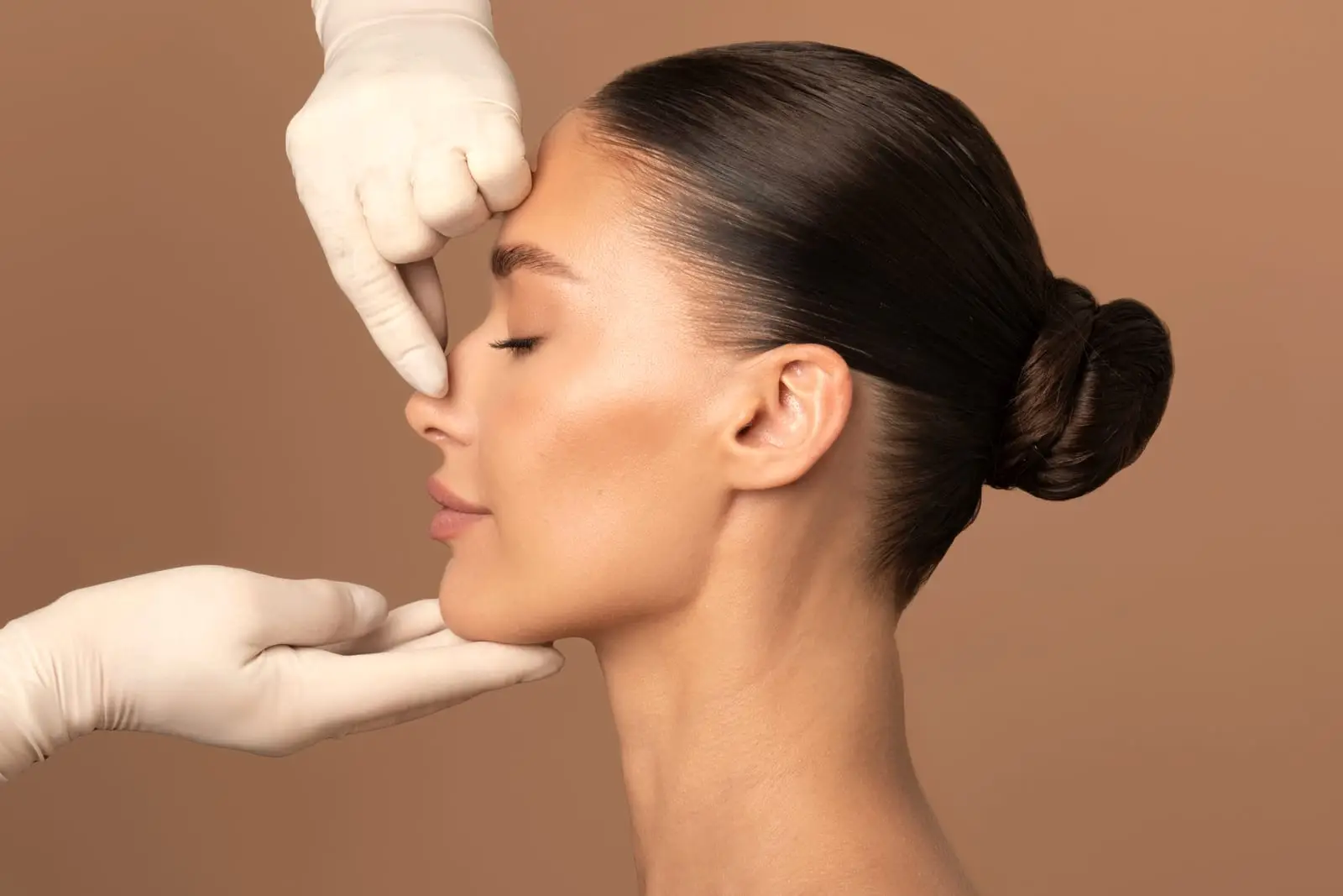 A woman in profile with two gloved hands framing her nose and jaw, in the position used to assess a nasal profile.